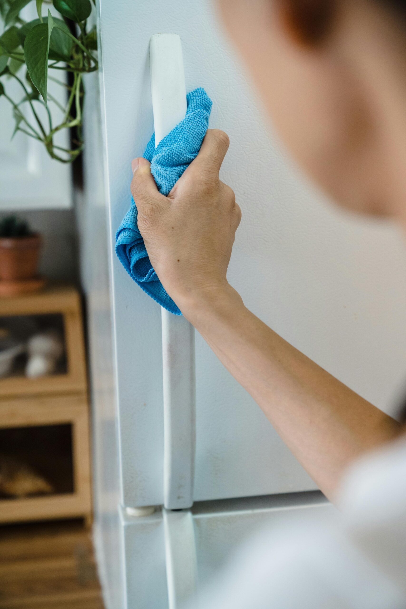 Close-up of a person cleaning a fridge handle with a blue cloth indoors.